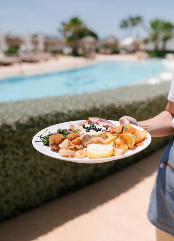 Camarera de Eques Petir Resort sirviendo un delicioso plato combinado en la zona de piscina.