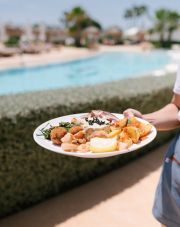 Camarera de Eques Petir Resort sirviendo un delicioso plato combinado en la zona de piscina.