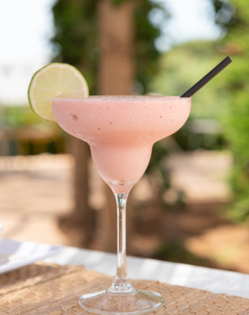 Refrescante cóctel rosa en copa alta, decorado con una rodaja de lima en el borde.