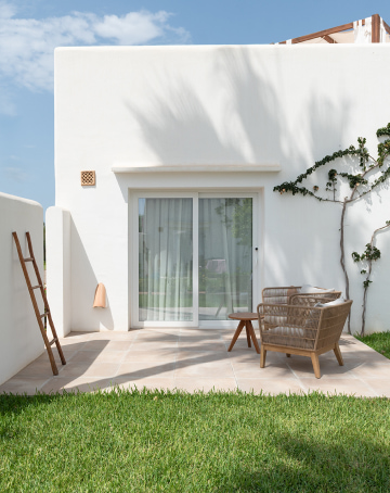 Terraza con sillas de mimbre y rodeada de jardines